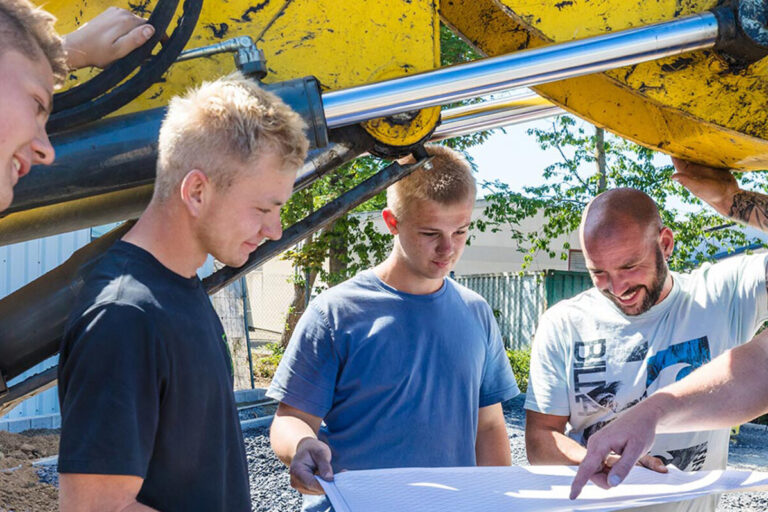 Ein Teil des Teams von Kötter Garten- und Landschaftsbau bei einer Besprechung unter einer Baggerschaufel