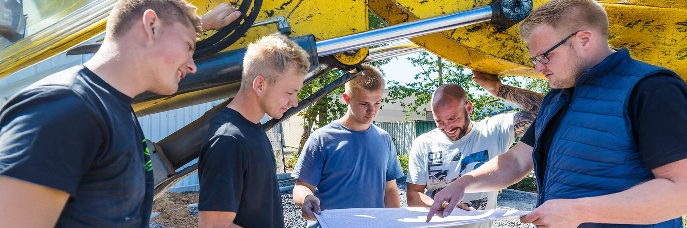 Ein Teil des Teams von Kötter Garten- und Landschaftsbau bei einer Besprechung unter einer Baggerschaufel